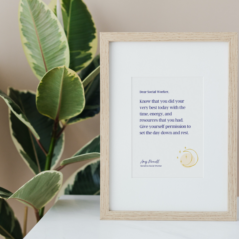 A white print sits in a wooden frame with a white mat. The font of the print is dark purple and reads "Dear Social Worker, Know that you did your very best today with the time, energy, and resources that you had. Give yourself permission to set the day down and rest. Amy Pinnell, Sensitive Social Worker". The frame is resting on a white table beside a green plant. 