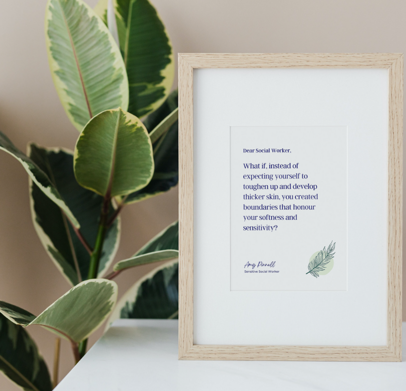 The print is shown in a wooden frame with a white mat. The print is white with purple font which reads "Dear Social Worker, What if, instead of expecting yourself to toughen up and develop thicker skin, you created boundaries that honour your softness and sensitivity? Amy Pinnell, Sensitive Social Worker". There is a dark green sketch of feather in the bottom right corner of the print. The frame sits on a white table beside a green plant.