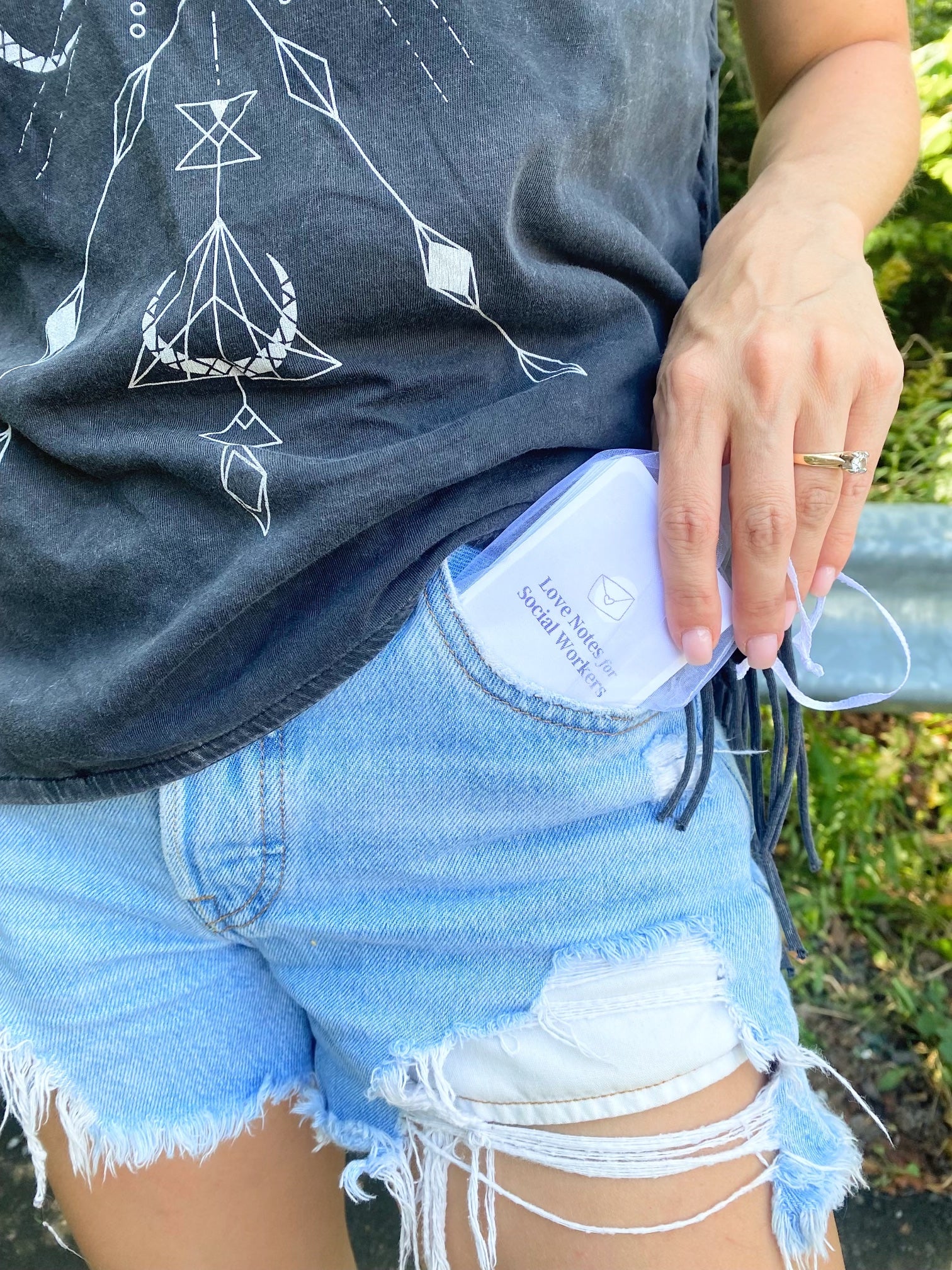 Women pulling card deck out of her jeans pocket to show the cover of the deck "Love Notes for Social Workers". 